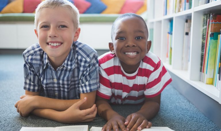 Portrait of school kids lying on floor reading book in library