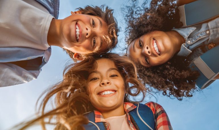 Portrait of smiling school kids standing in cecrle at school yard with look in camera